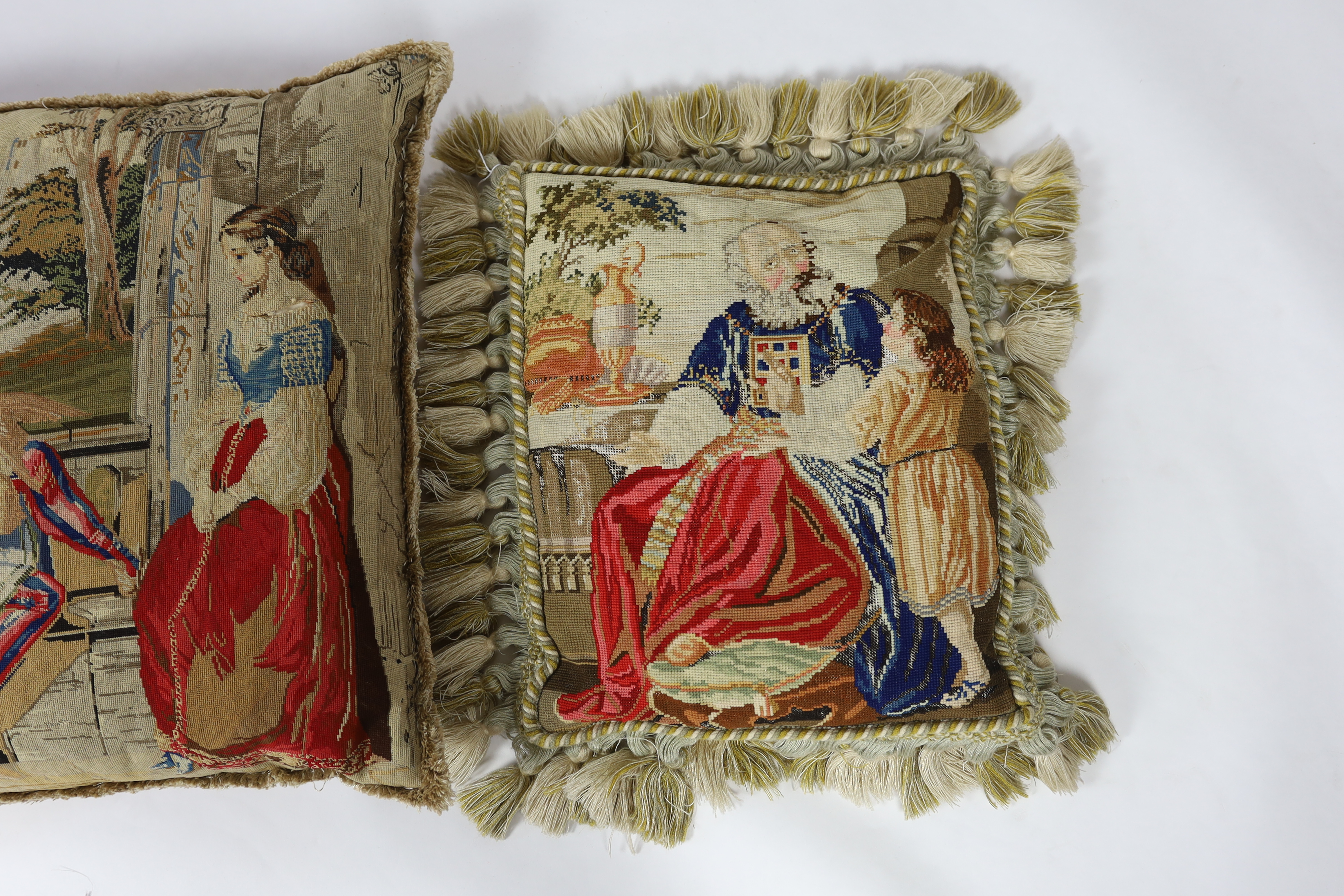 Three Victorian Berlin wool worked cushions possibly of classical biblical scenes, all three cushions edged with braiding and fringing, largest cushion 61cm wide, 65cm high